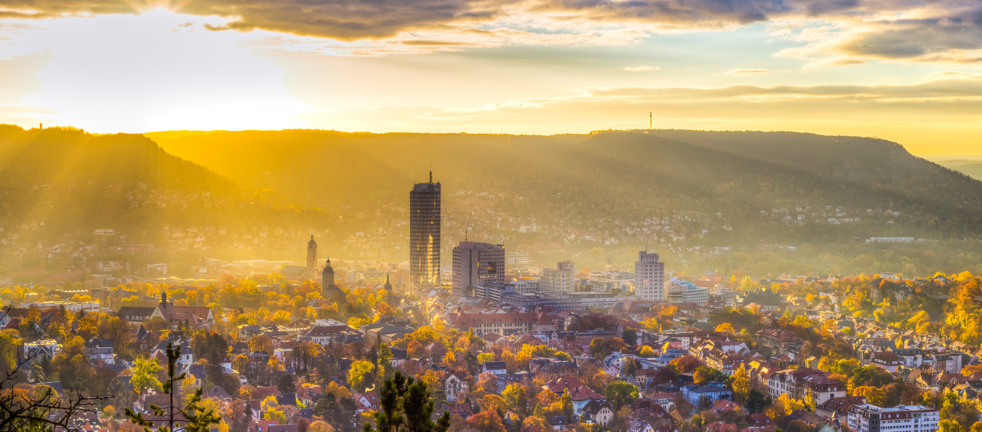 Sonnenuntergang über der Stadt Jena mit Blick auf den Jentower, Kirchturm und bewaldete Hügel im Hintergrund