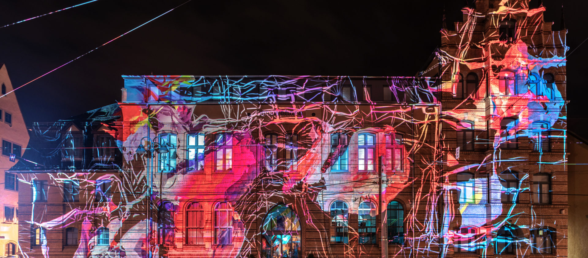 Historisches Gebäude in Jena bei Nacht mit farbiger Lichtprojektion und abstrakten Linienmustern auf der Fassade