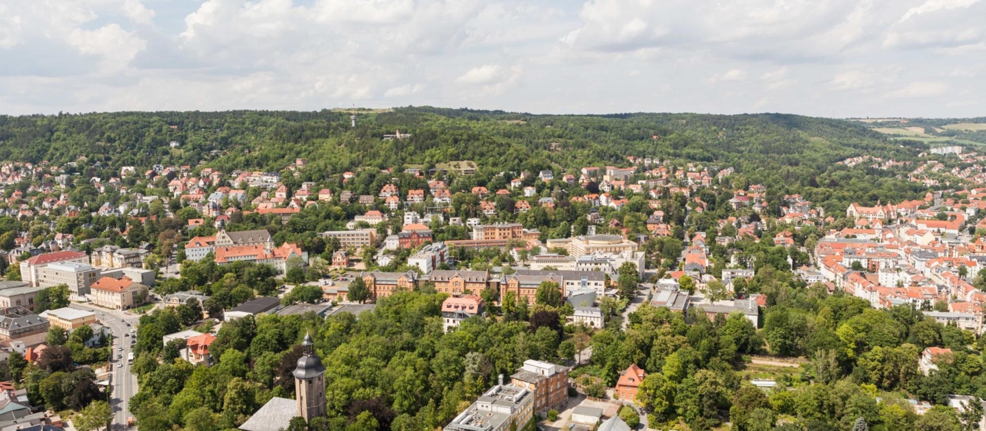 Blick vom Jentower auf die Stadt Jena mit vielen Bäumen, Wohnhäusern und im Vordergrund die Friedenskirche