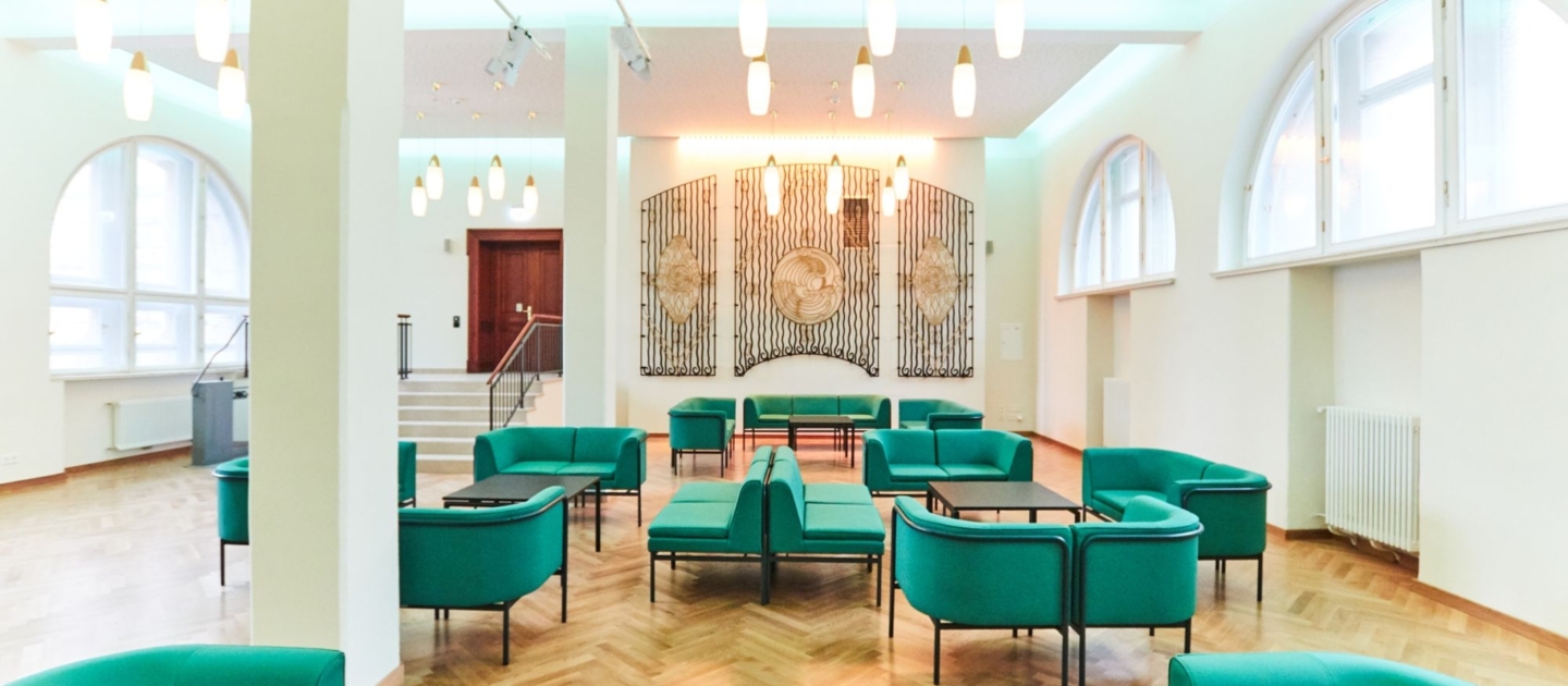 Sitzbereich mit grünen Sesseln und Sofas im Schaeffersaal des Volkshauses Jena, helle Wände, große Fenster und dekorative Wandkunst