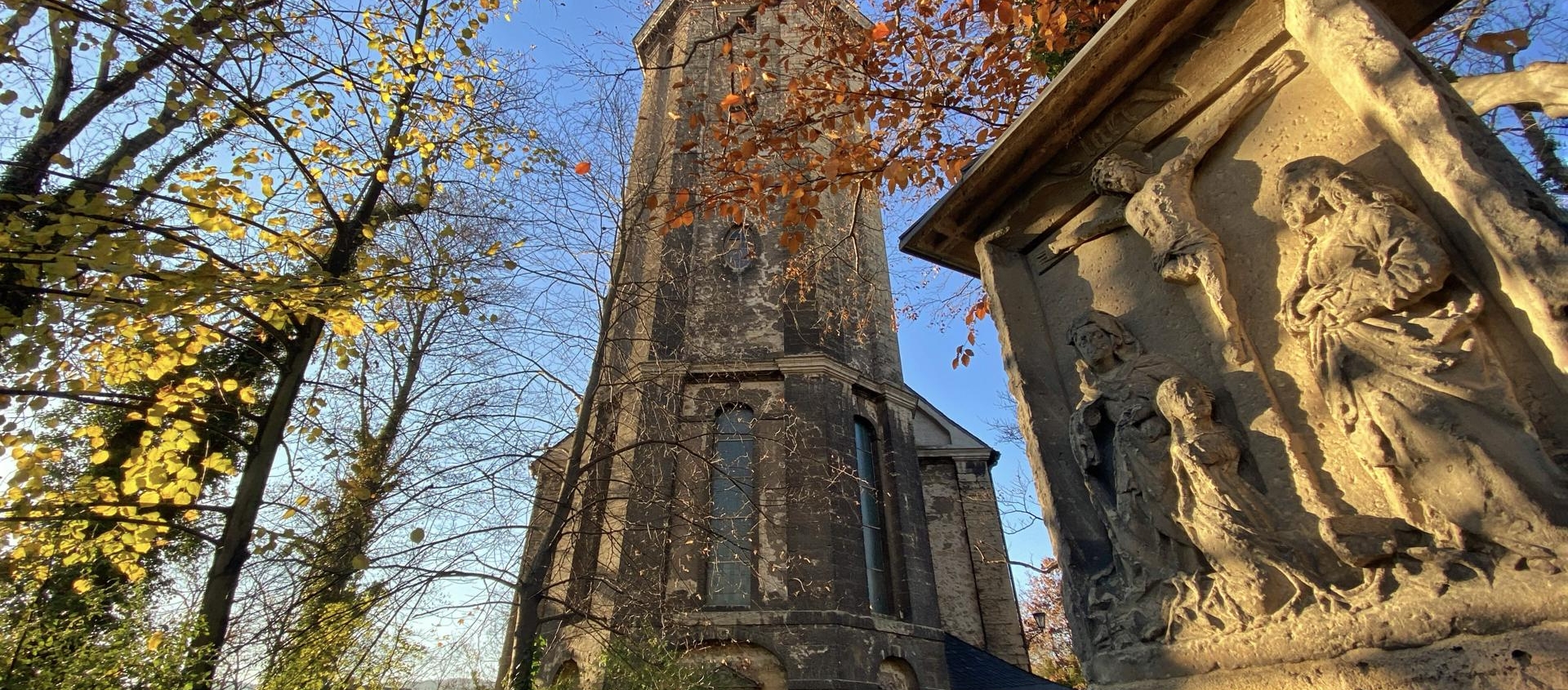 Friedenskirche in Jena mit herbstlichen Bäumen und steinerner Reliefskulptur im Vordergrund
