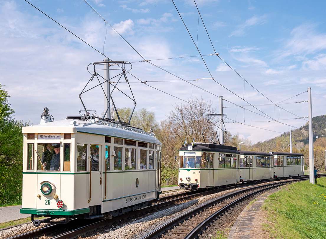 Historischer Triebwagen mit der Nummer 26 und historischer Dreiwagenzug auf einer Gleisstrecke im Freien unter Oberleitungen in Jena