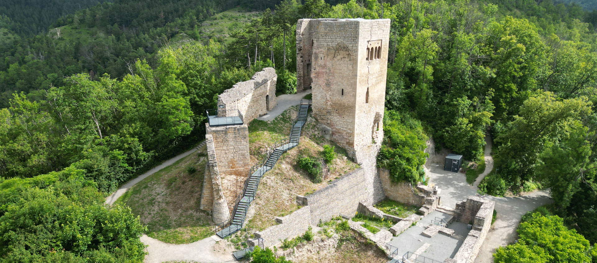 Luftaufnahme der Ruine der Lobdeburg mit einem hohen rechteckigen Turm und umgebenden Mauern, umgeben von dichtem Wald bei Jena
