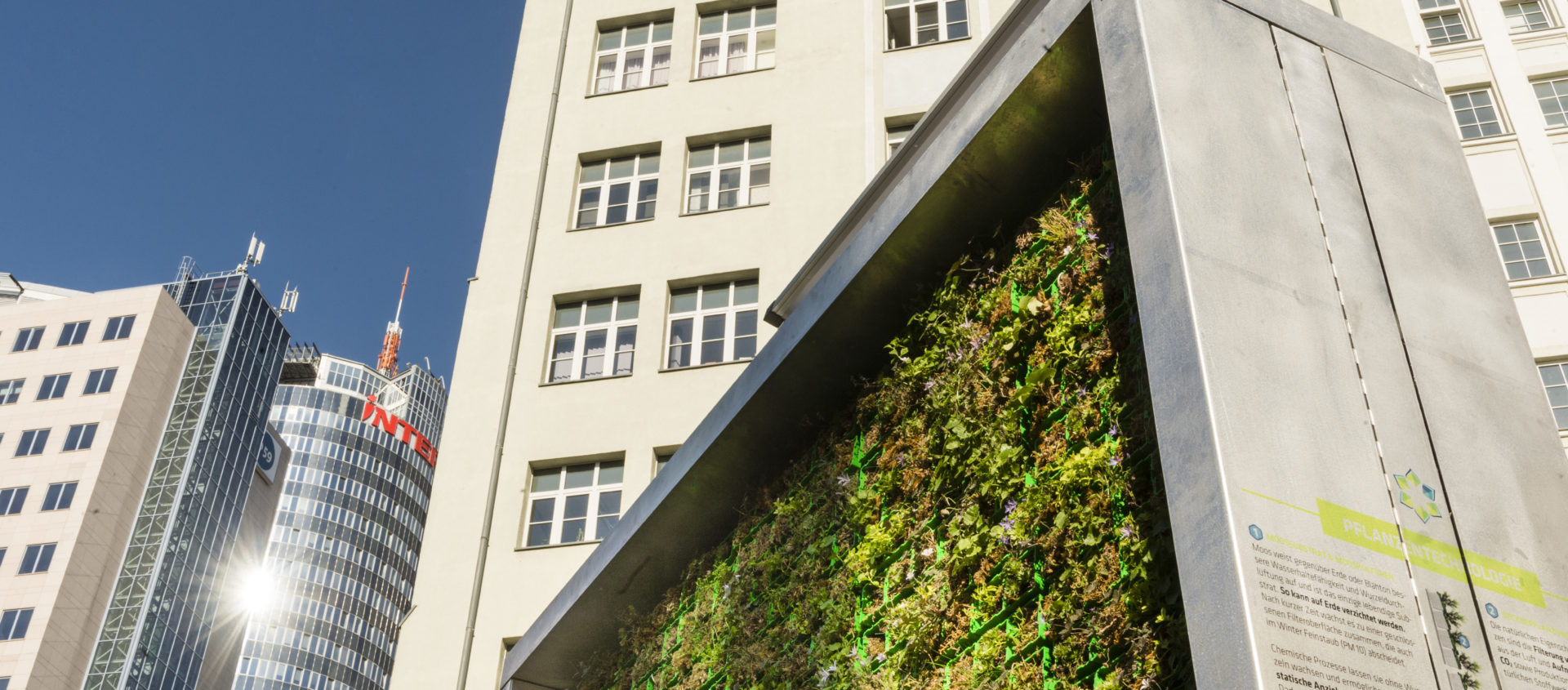 Blick auf ein modernes Bürogebäude und im Vordergrund eine vertikale Begrünungswand mit Pflanzen vor blauem Himmel in Jena.