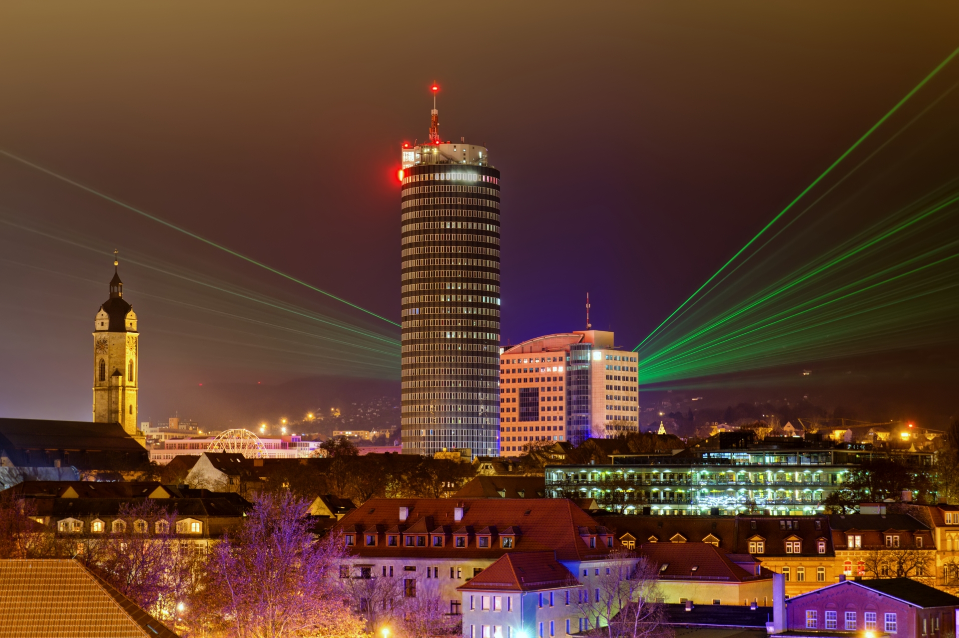 Nächtliche Stadtansicht von Jena mit dem markanten JenTower und grünen Laserscheinwerfern am Himmel zur Langen Nacht der Wissenschaften