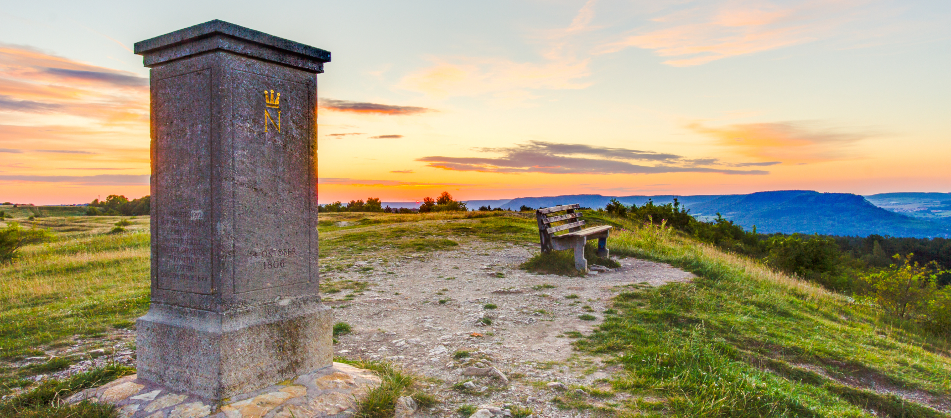 Der Napoleonstein auf dem Windknollen bei Dämmerung mit einer Bank und weiter Landschaft im Hintergrund