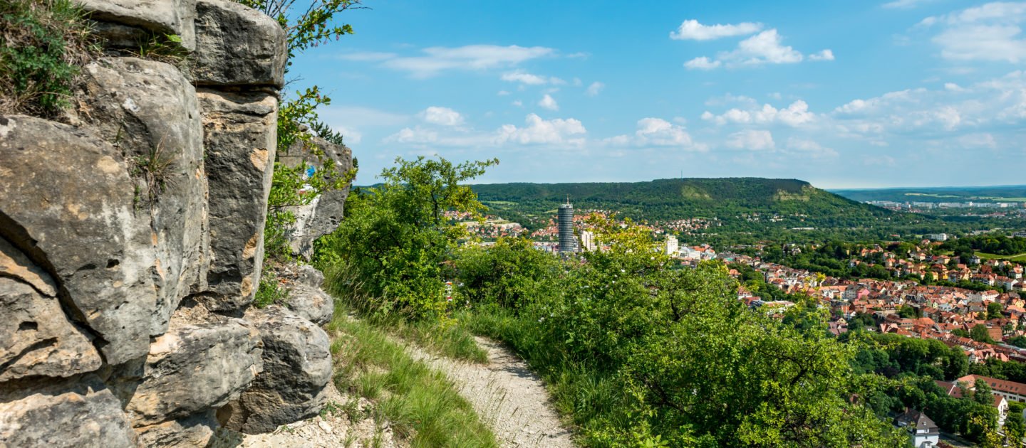 Wanderweg SaaleHorizontale an einer felsigen Steilkante mit Blick auf Jena unter blauem Himmel