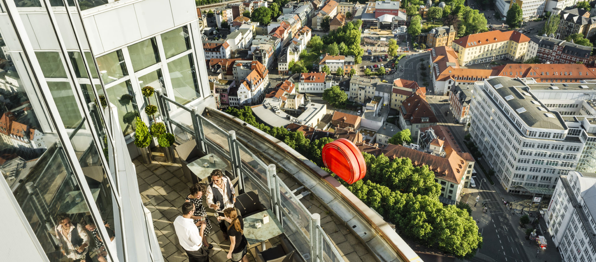 Blick auf die Jentower-Aussichtsplattform auf eine Gruppe von Menschen und die darunter liegende Stadt mit Gebäuden und viel Grün