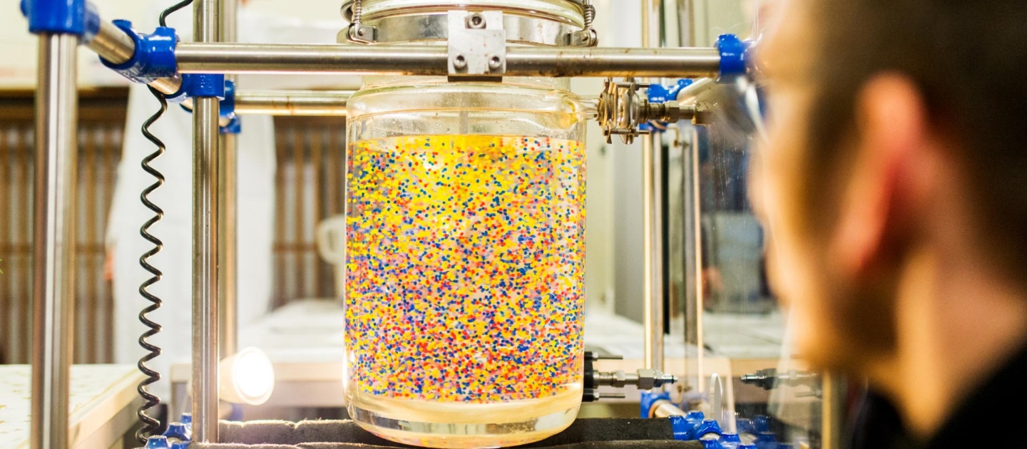 Experiment mit einem Glaszylinder gefüllt mit gelber Flüssigkeit und bunten Partikeln bei der Langen Nacht der Wissenschaften in Jena