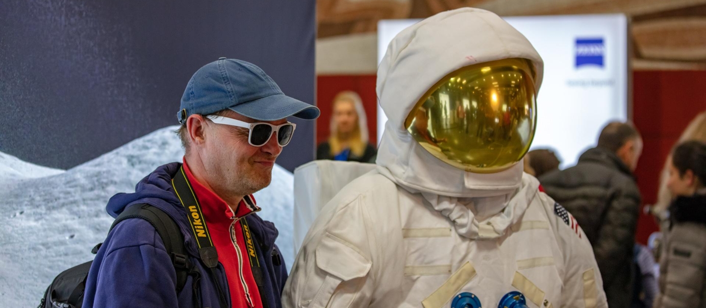 Besucher mit blauer Kappe und rotem Pullover neben Person im weißen Raumanzug mit goldfarbenem Visier bei der Langen Nacht der Wissenschaften in Jena