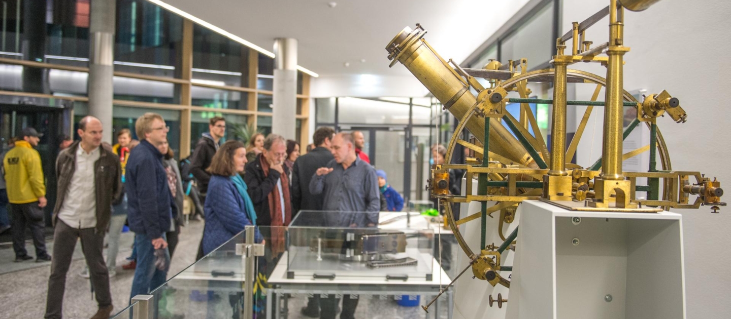 Historisches wissenschaftliches Messgerät aus Messing im Vordergrund, Besuchergruppe bei der Langen Nacht der Wissenschaften in Jena im Hintergrund