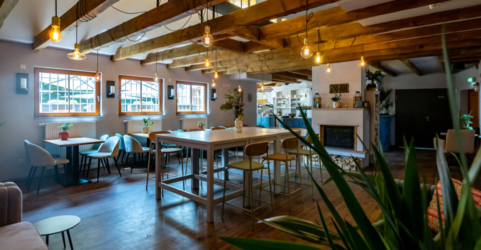 Paradiescafe-Jena-innen-Bernd-Widemann Innenraum des Paradiescafés in Jena mit Holzbalkendecke, mehreren Tischen und Stühlen, Pflanzen und warmen Hängelampen.