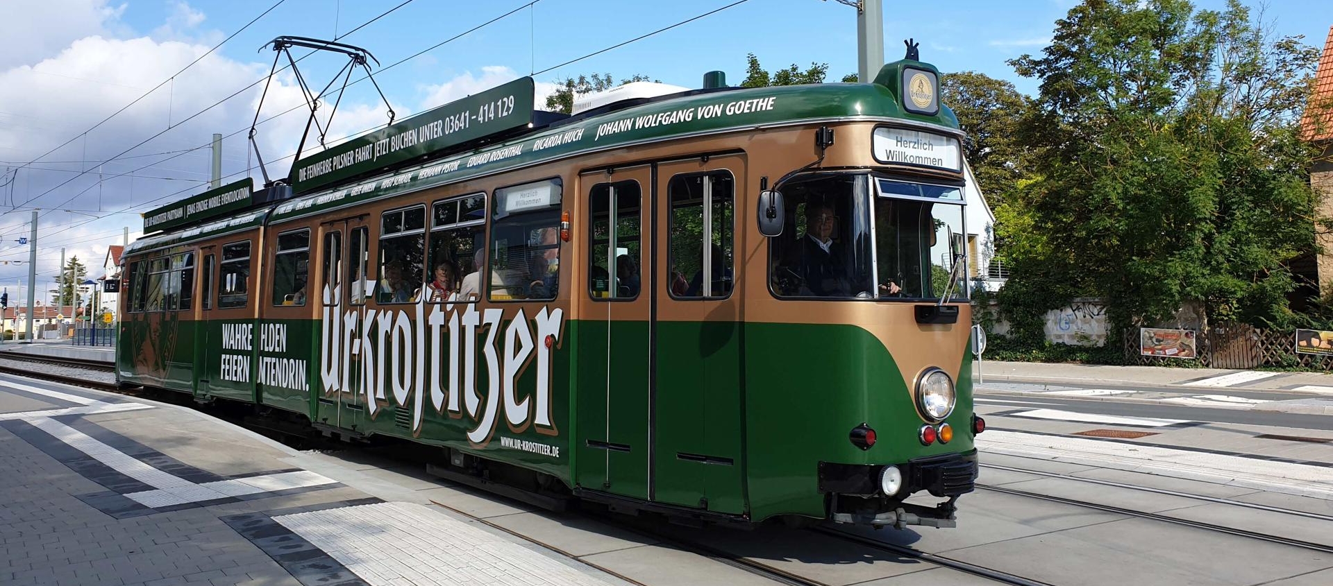 Grüne historische Straßenbahn der Partybahn Jena mit Werbung für Ur-Krostitzer fährt auf Gleisen im Nahverkehr