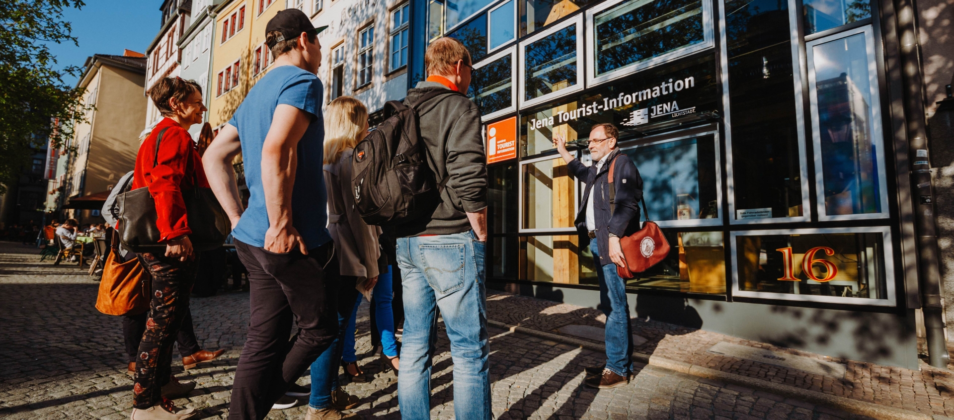 Gruppe von Touristen hört einem Stadtführer vor der Jena Tourist-Information zu, sonniger Tag