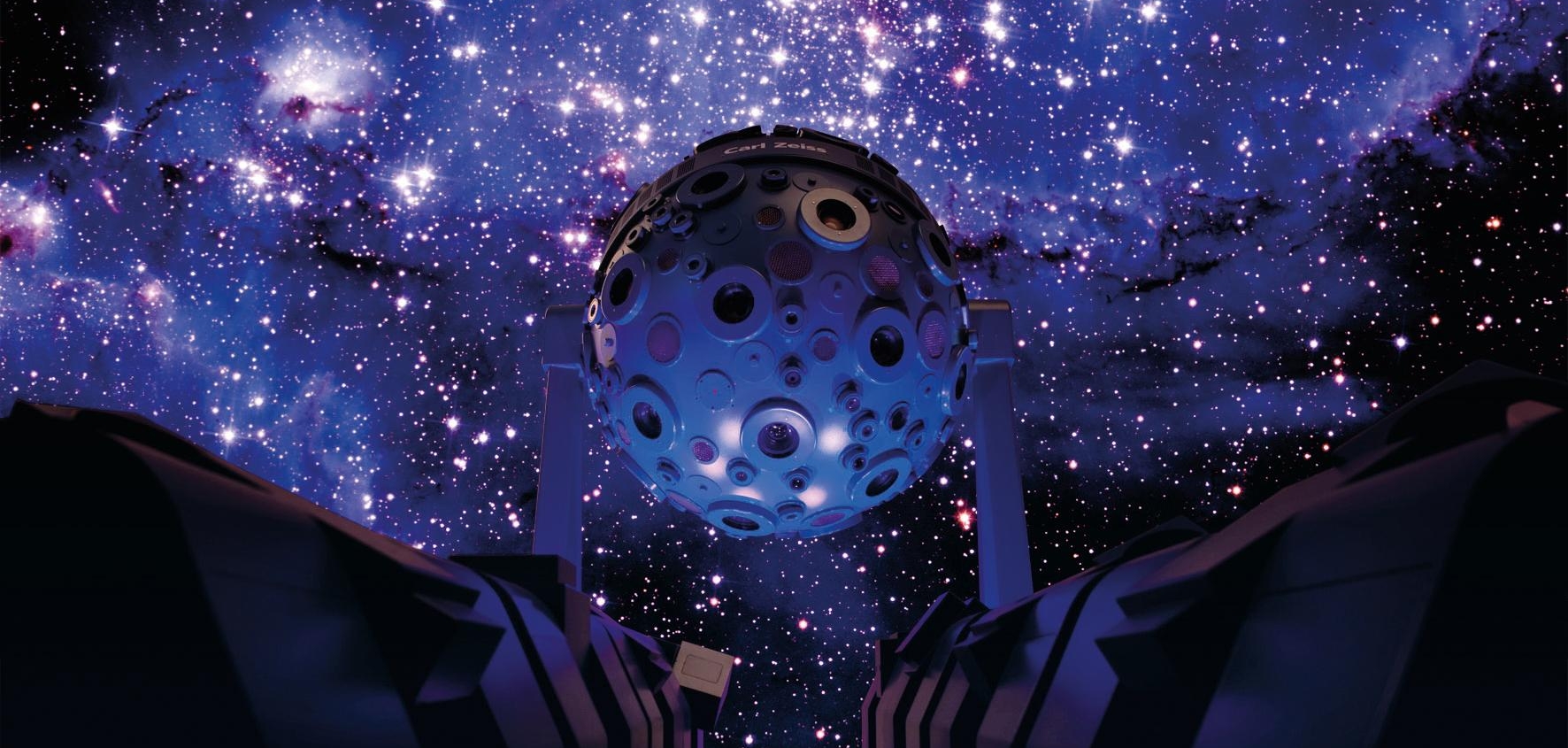 Kugelförmiger Sternprojektor mit zahlreichen runden Öffnungen vor einem Sternenhimmel im Zeiss-Planetarium Jena