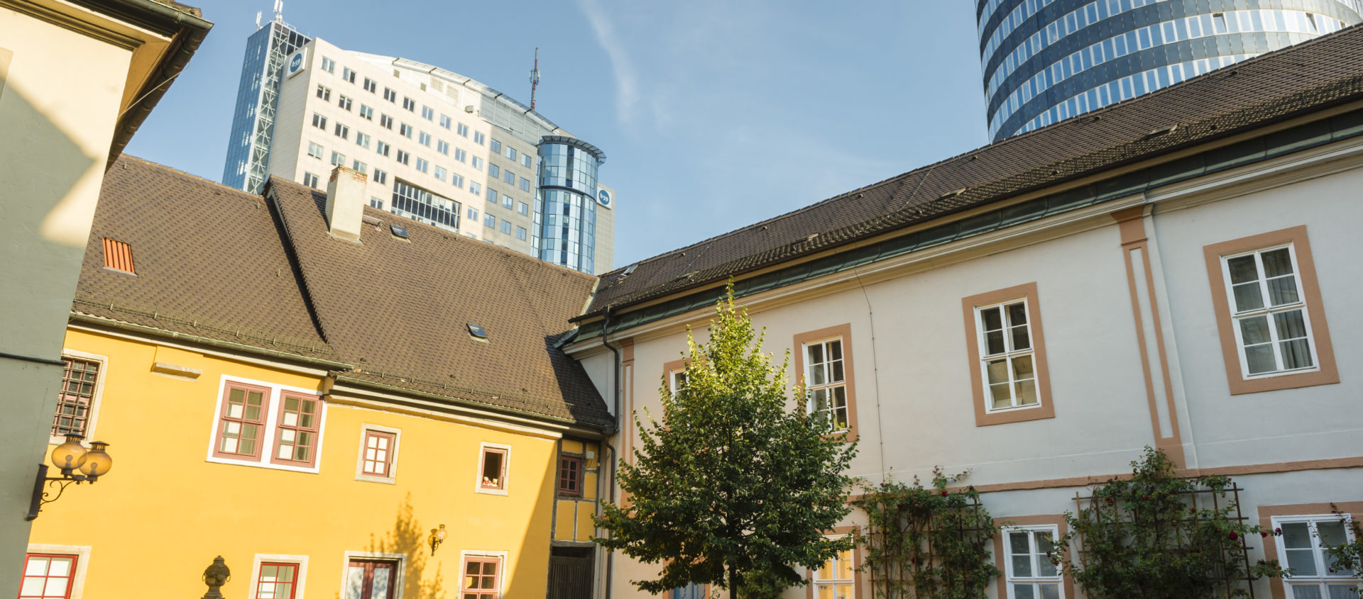 Innenhof des Collegium Jenense mit historischen Gebäuden und moderner Hochhauskulisse im Hintergrund