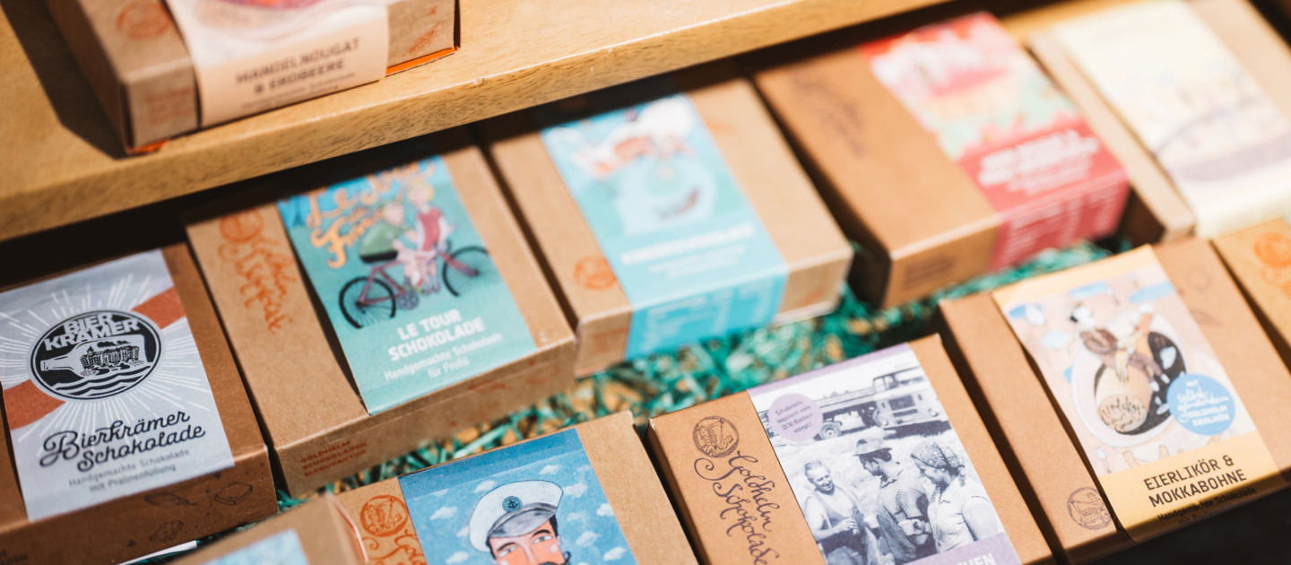 Verschiedene Schokoladen von Goldhelm in braunen Verpackungen mit bunten Etiketten, ausgestellt in der Jena Tourist-Information