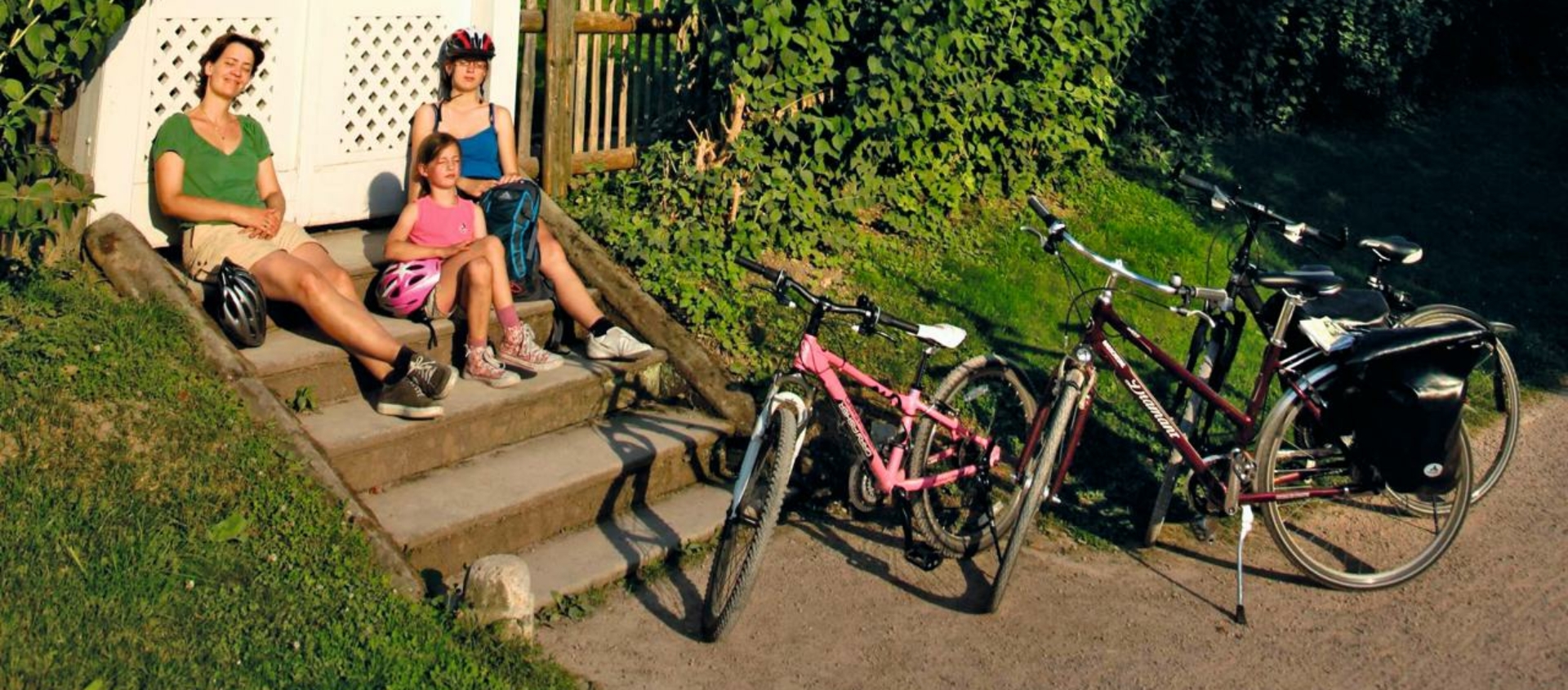 Goethes Gartenhaus in Weimar mit spitzem Dach und Kletterpflanzen, davor eine Gruppe von Menschen auf einer Treppe neben mehreren Fahrrädern und einem weißen Gartenpavillon