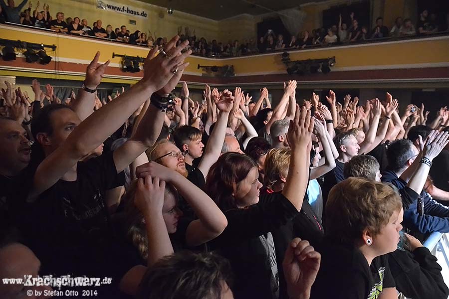 Publikum in einem Konzertsaal mit erhobenen Händen und applaudierend, im Hintergrund ein Balkon mit weiteren Zuschauern