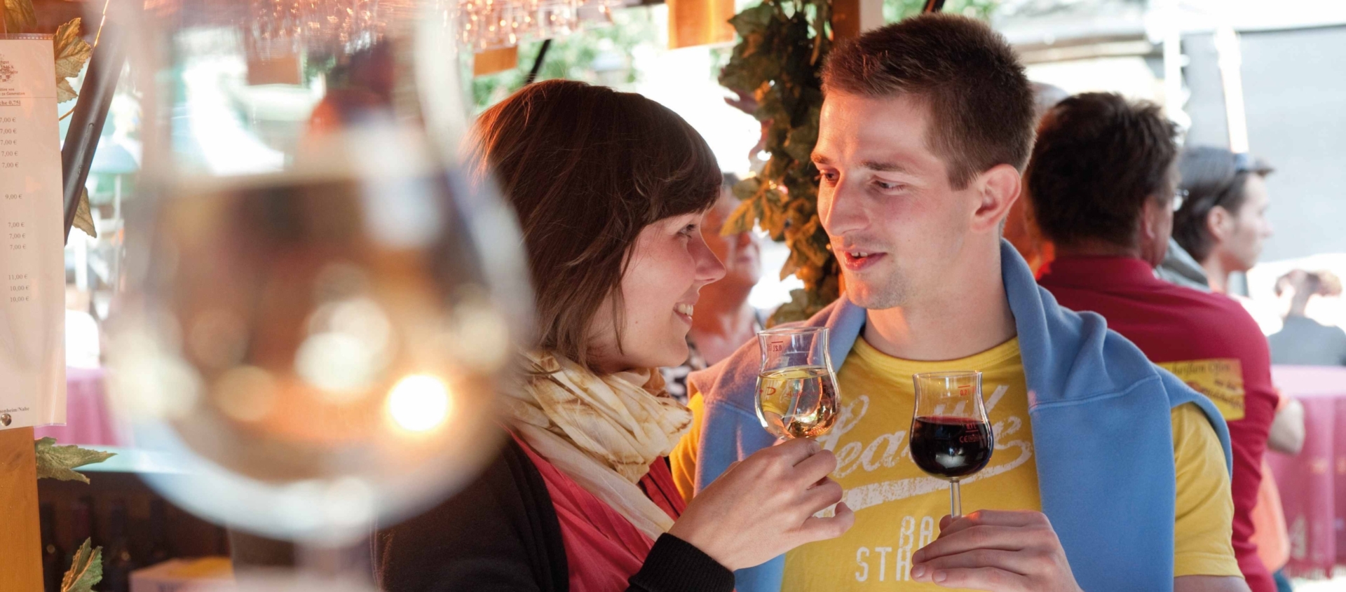 Zwei Personen stoßen mit Weingläsern an, im Vordergrund unscharf ein weiteres Weinglas