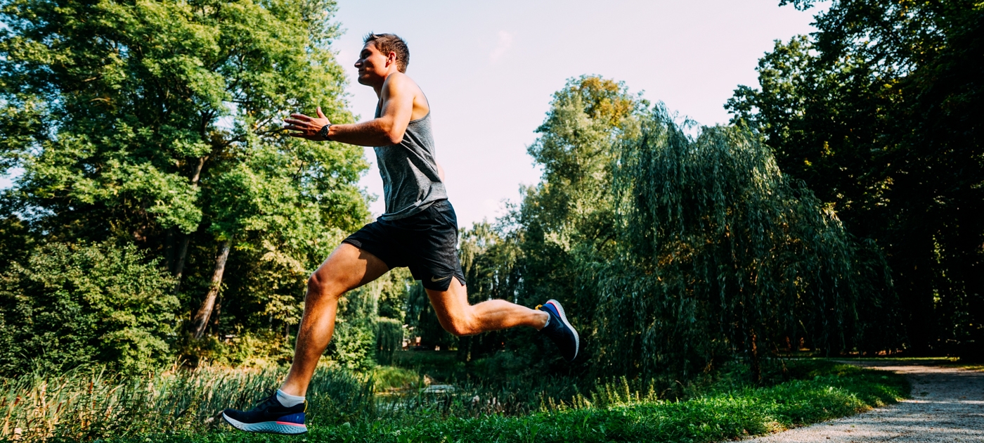 Mann in Sportkleidung springt im Jenaer Paradiespark über einen Weg, umgeben von Bäumen und Grünflächen
