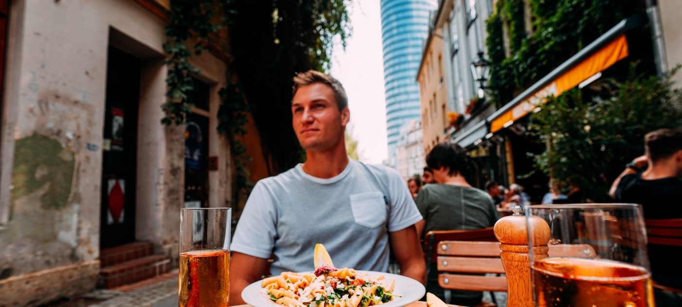 Blick auf einen gedeckten Tisch mit Brot, Salat und Getränken in der Wagnergasse in Jena, im Hintergrund Straßencafés und der JenTower.