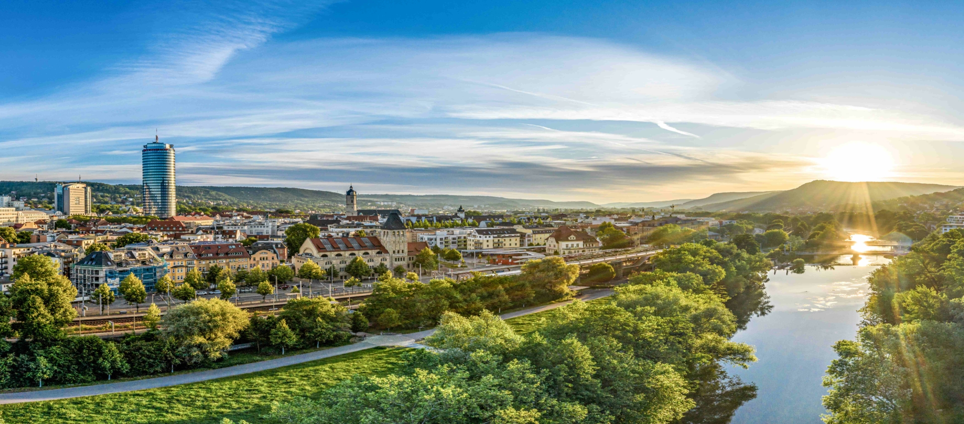 Panorama der Stadt Jena mit der Saale, grünen Uferbereichen und der aufgehenden Sonne am Horizont