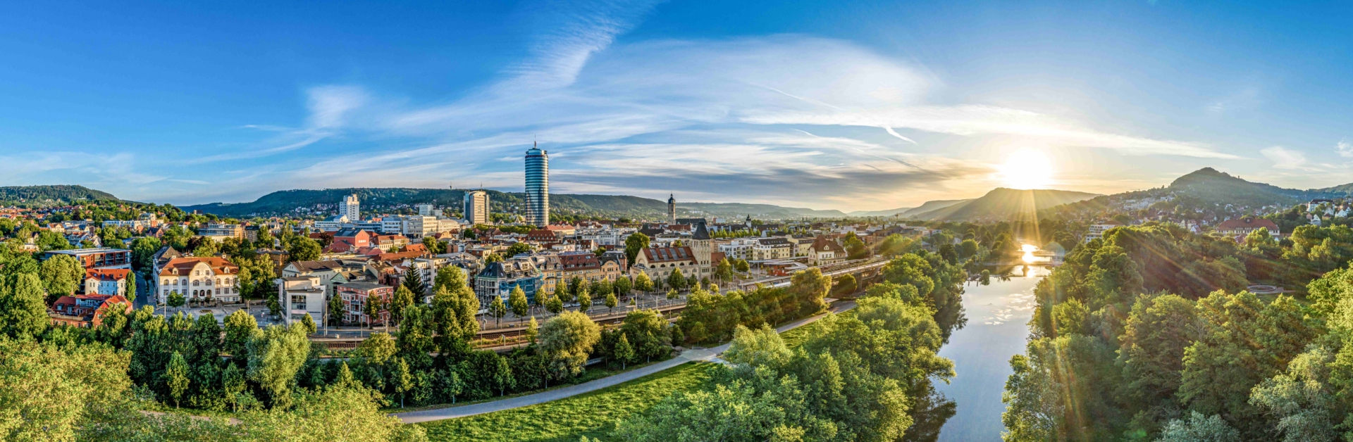 Panorama der Stadt Jena mit der Saale, grünen Uferbereichen und der aufgehenden Sonne am Horizont