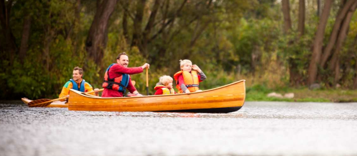 Familie mit mehreren Personen in einem gelben Kanu auf der Saale in Jena umgeben von Bäumen und Wasser