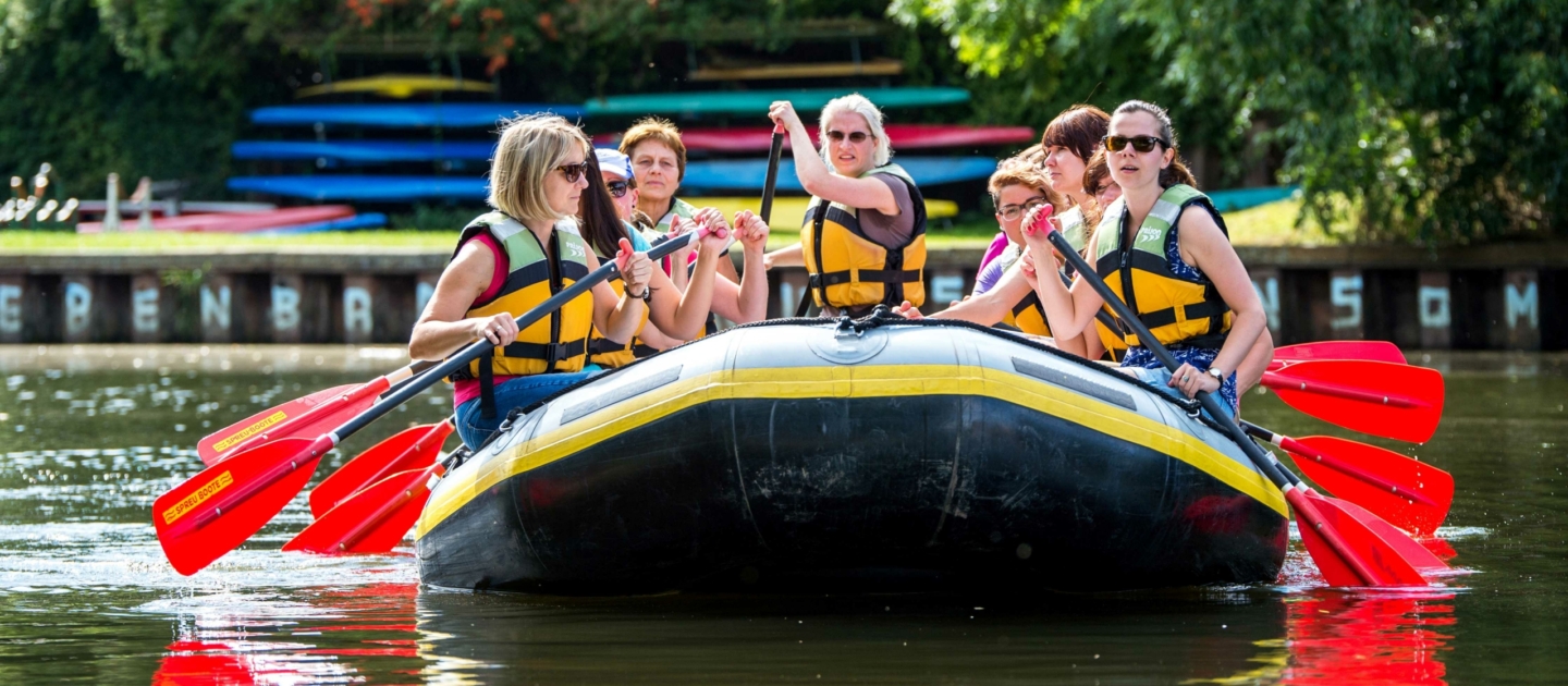 Gruppe von Personen mit Schwimmwesten paddelt in einem Schlauchboot auf der Saale in Jena