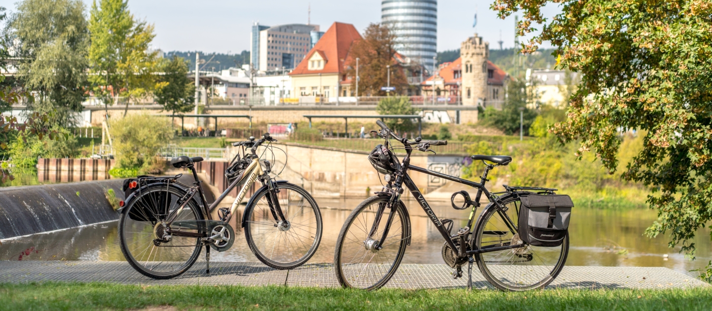 Zwei Fahrräder stehen auf einer Wiese am Ufer der Saale mit Blick auf den markanten Jentower in Jena