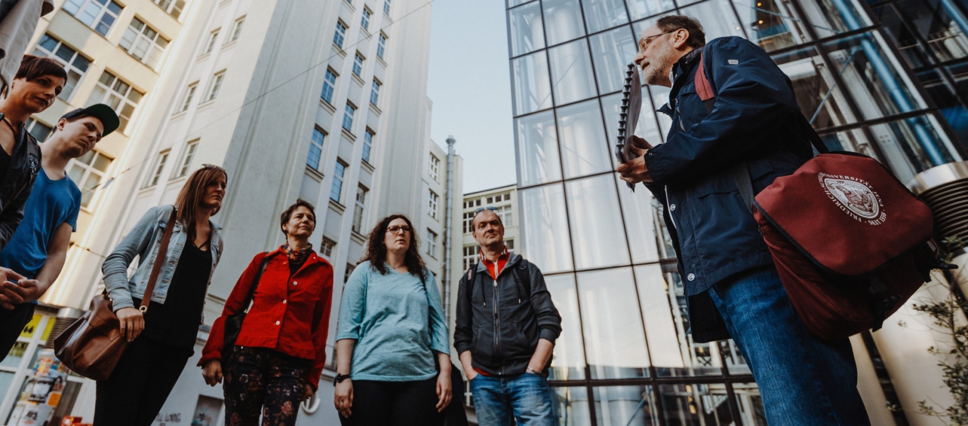 Gruppe von Menschen steht im Kreis auf einem Platz umgeben von hohen modernen und historischen Gebäuden in Jena