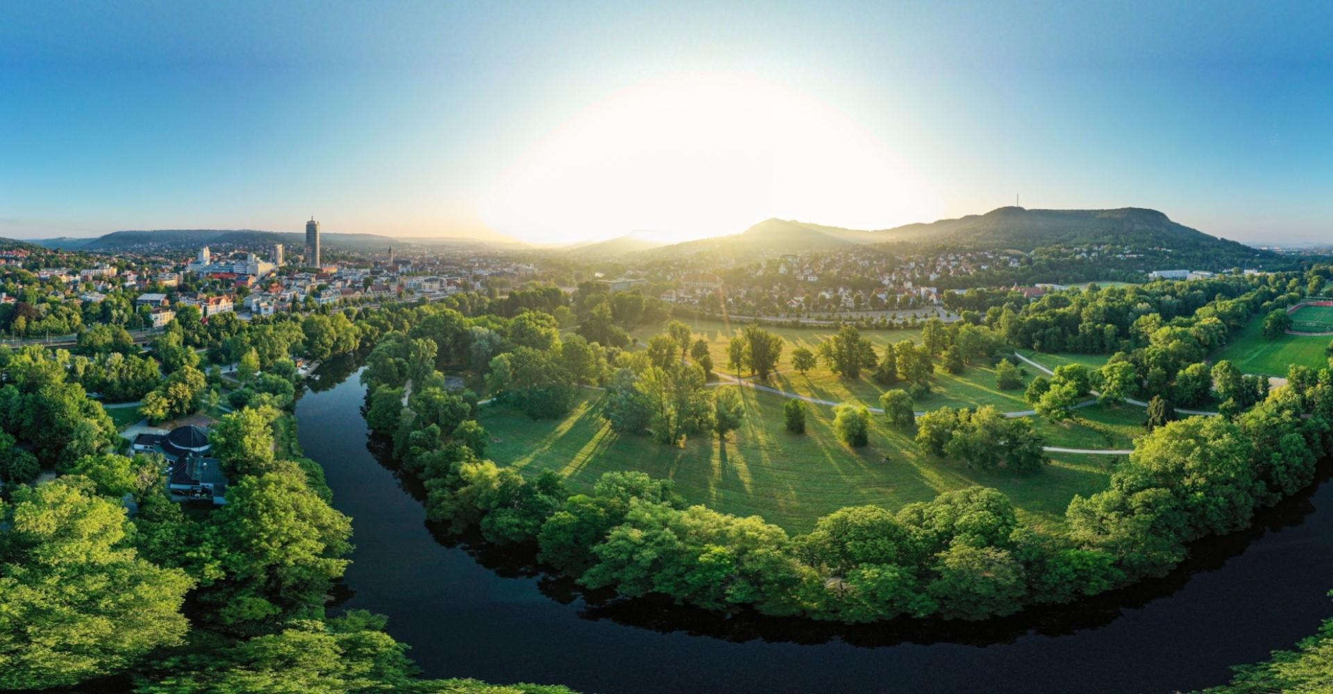 Panoramablick auf die Saaleaue in Jena mit Fluss, grünen Wiesen und Stadt im Hintergrund bei Sonnenaufgang