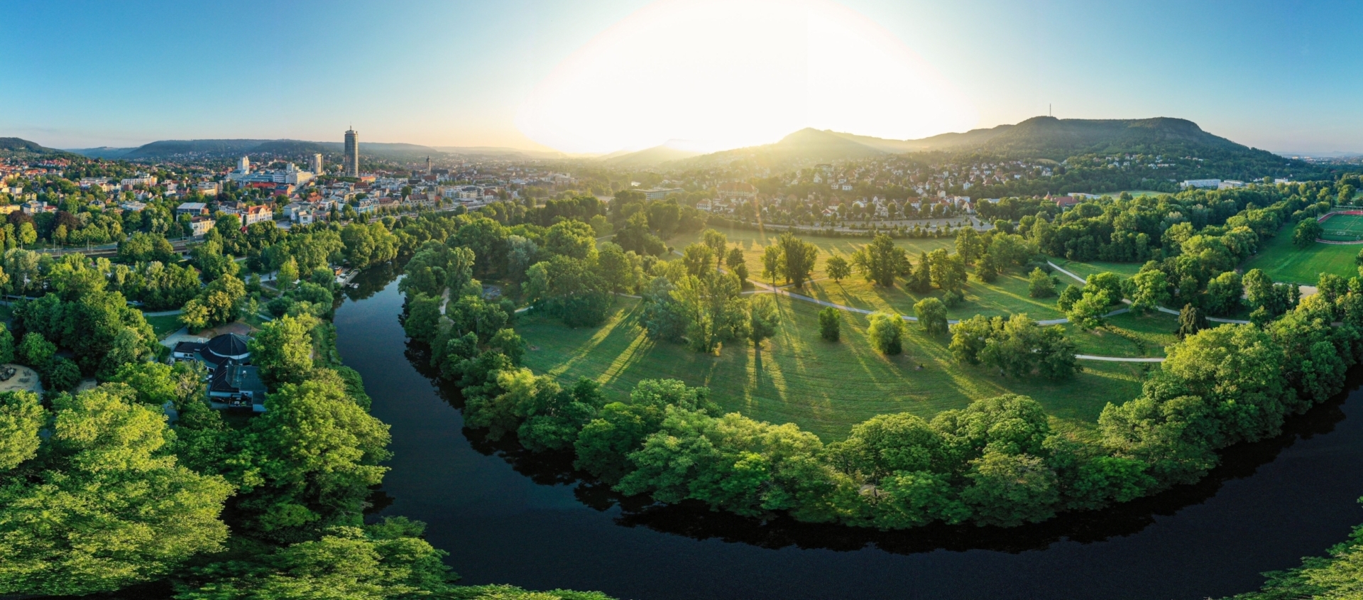 Panoramablick auf die Saaleaue in Jena mit Fluss, grünen Wiesen und Stadt im Hintergrund bei Sonnenaufgang
