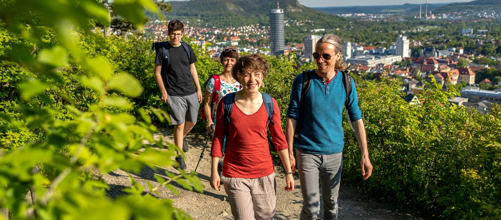 Vier Wanderer auf dem Wanderweg Saalehorizontale mit Blick auf die Stadt Jena und den markanten JenTower im Hintergrund