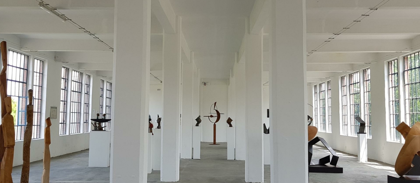 Innenraum des Eiermannbaus in Apolda mit weißen Säulen und mehreren modernen Skulpturen auf Podesten entlang der Seitenwände und in der Mitte des Raums