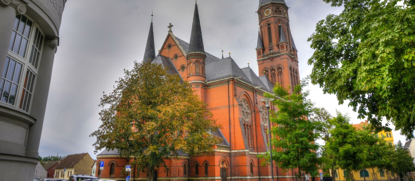 Die Lutherkirche in Apolda mit markanten roten Backsteinmauern und mehreren spitzen Türmen unter bewölktem Himmel