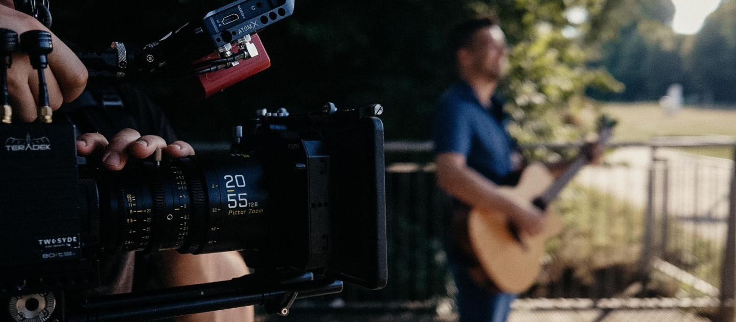 Kameramann filmt einen Mann mit Gitarre im Freien, unscharfer Hintergrund mit Zaun und Bäumen in Jena