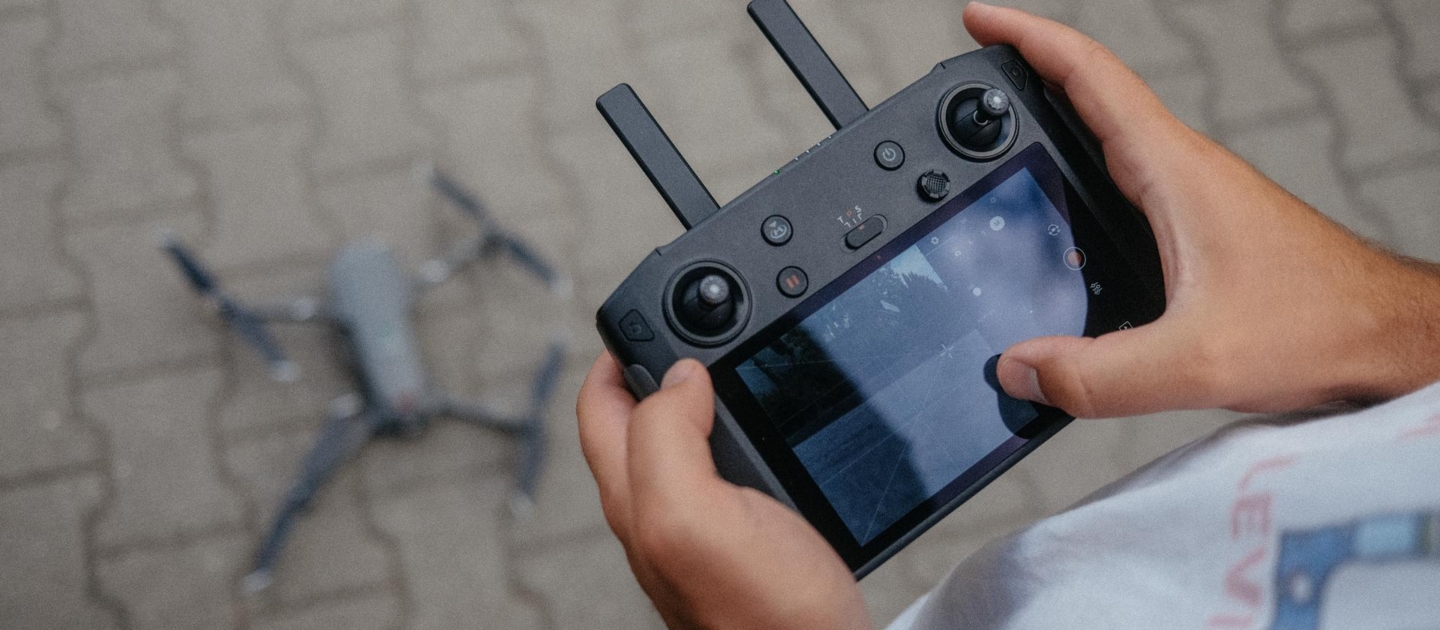 Person steuert eine Drohne mit einer Fernbedienung mit Bildschirm auf gepflastertem Boden in Jena