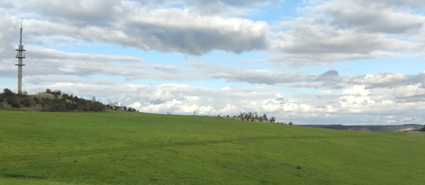 Grüne Hügel bei Jena mit einem Sendemast auf einem Hügel unter bewölktem Himmel