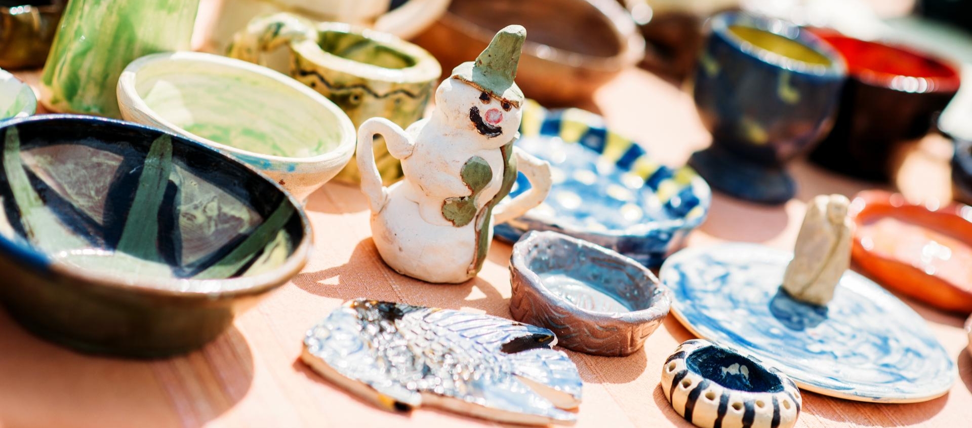 Verschiedene handgefertigte Keramikstücke auf einem Tisch beim Töpfermarkt in Jena, darunter bunte Schalen, Tassen und eine kleine Schneemannfigur.