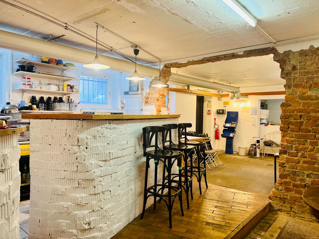 Innenraum einer Galerie in Jena mit weiß gestrichenem Backsteinbar, drei schwarzen Barhockern und sichtbaren Ziegelwänden