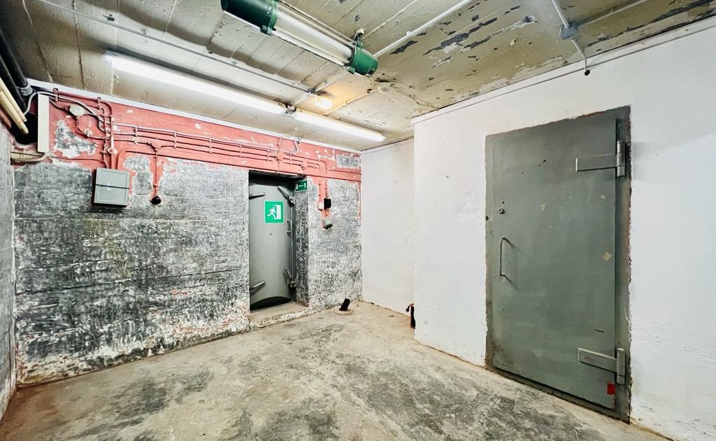 Raum in einer Galerie in Jena mit roher Betonwand, grauer Stahltür und Notausgangsschild über einer weiteren Tür