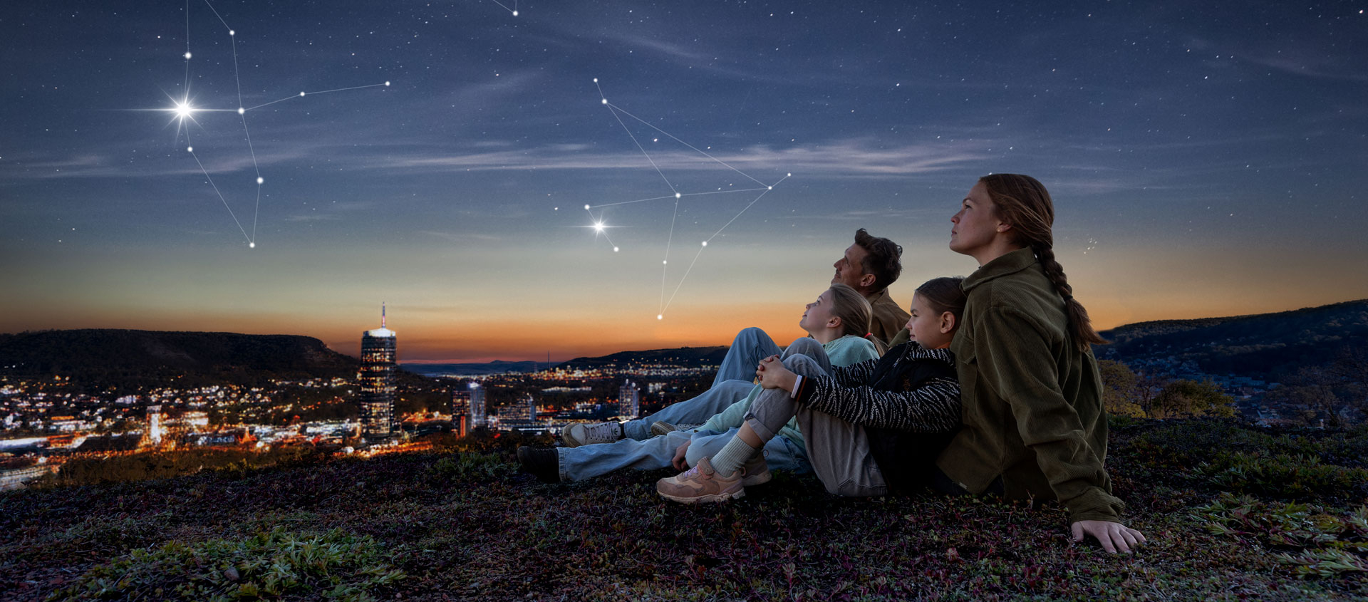Familie sitzt auf einer Anhöhe über Jena und blickt in den Abendhimmel mit hervorgehobenen Sternbildern